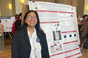Smiling woman in a blazer with a lanyard stands beside a large scientific poster at a conference.