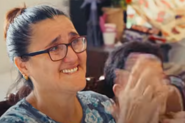 Smiling woman with glasses and dark hair in a bun, wearing a floral top, clapping beside her.