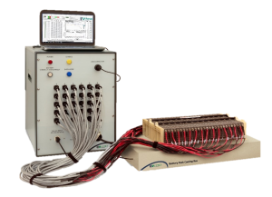 Industrial battery testing rack connected to a laptop, showing graphs on screen (multi‑wire harnesses and control panel).